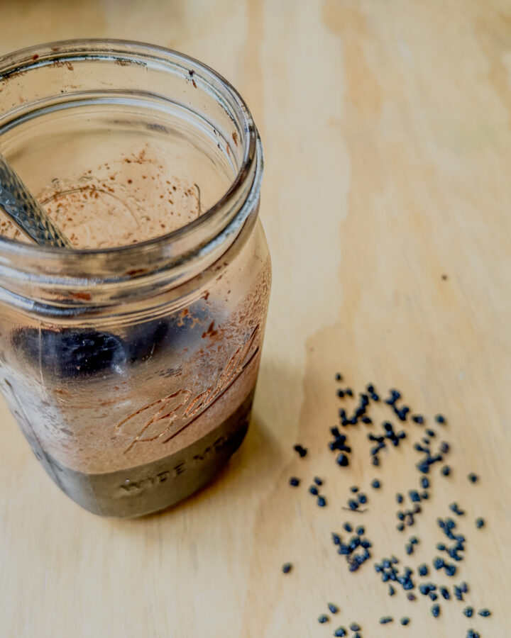 elderberry in syrup in a jar on a table with a spoon and dried berries around it