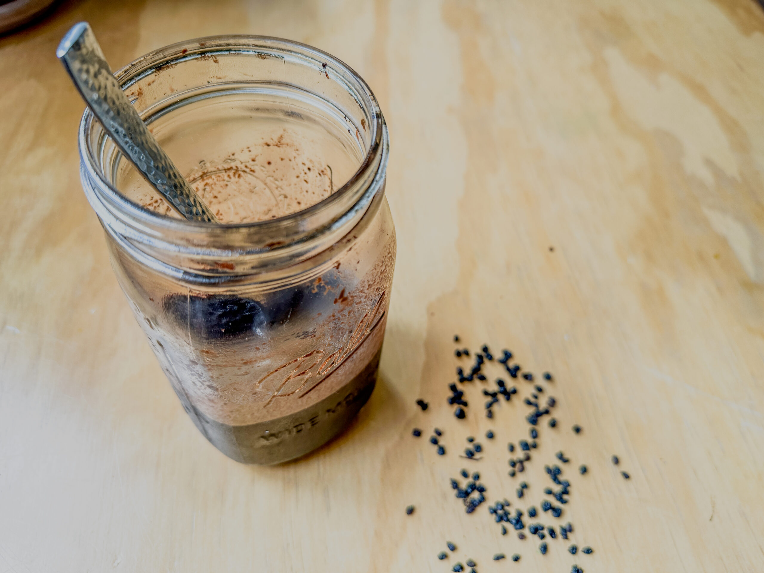 elderberry in syrup in a jar on a table with a spoon and dried berries around it